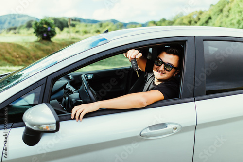 Young man in sunglasses sitting in car holding car keys outdoors