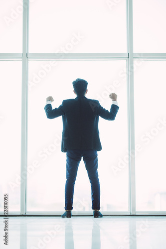 Young successful businessman with raised arms in front of the city on panoramic windows