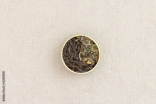 Leaves of black and white tea in a round form on a fabric laid out as a sign of yin and yang