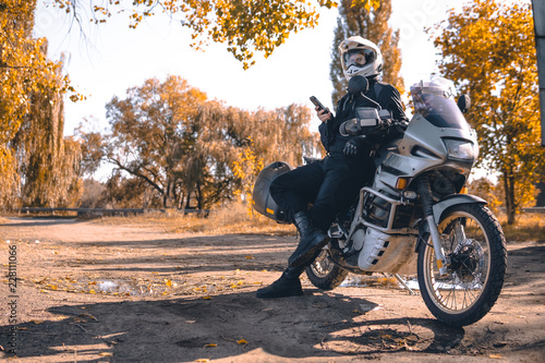 Fototapeta Naklejka Na Ścianę i Meble -  Motorbiker travelling, autumn day, motorcycle off road, rider, adventurer, extreme tourism, cold weather clothes, yellow forest, copy space, uses smartphone, internet, search,