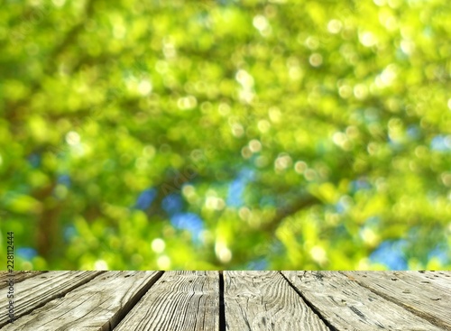The old wooden table in foreground with blur background of bokeh and many green leaves are blooming in the garden, montage style 