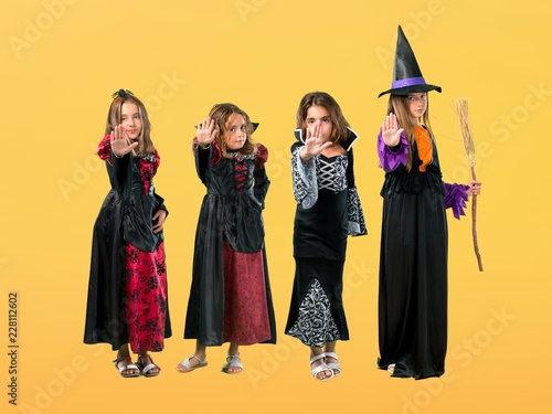Set of Little girl dressed as a vampire for halloween holidays making stop gesture with her hand on orange background