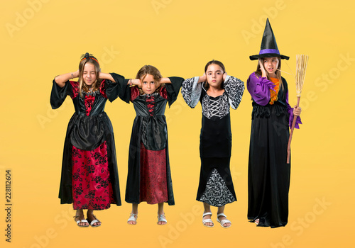 Set of Little girl dressed as a vampire for halloween holidays covering both ears with hands on orange background