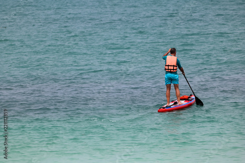 Tourist man enjoying the stand up paddle board or surfboard on the tropical beach