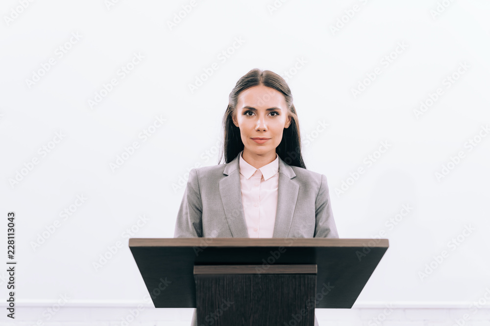 attractive lecturer standing at podium tribune during seminar in conference hall and looking at camera attractive lecturer standing at podium tribune during seminar in conference hall and looking at camera