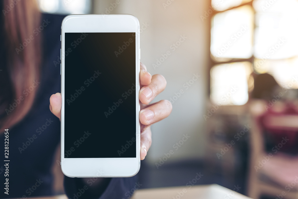 Mockup image of a woman holding and showing white mobile phone with blank screen in cafe Mockup image of a woman holding and showing white mobile phone with blank screen in cafe