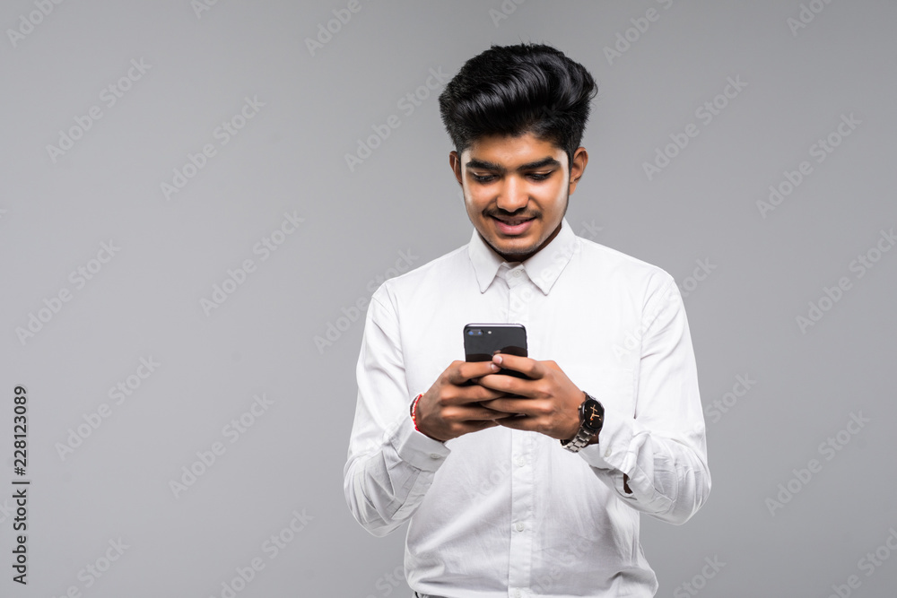 Young happy Indian Sikh man using mobile phone isolated against gray background Young happy Indian Sikh man using mobile phone isolated against gray background