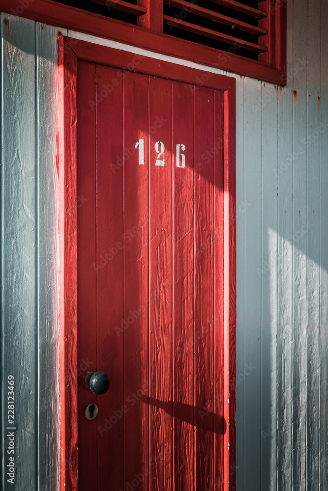 Numbered red door. Beautiful seaside holiday Bathing houses on sandy beach. Empty shelters on a sunny but moody day. Summer architecture, colored paint, maze like labyrinth. Numbered red door. Beautiful seaside holiday Bathing houses on sandy beach. Empty shelters on a sunny but moody day. Summer architecture, colored paint, maze like labyrinth.