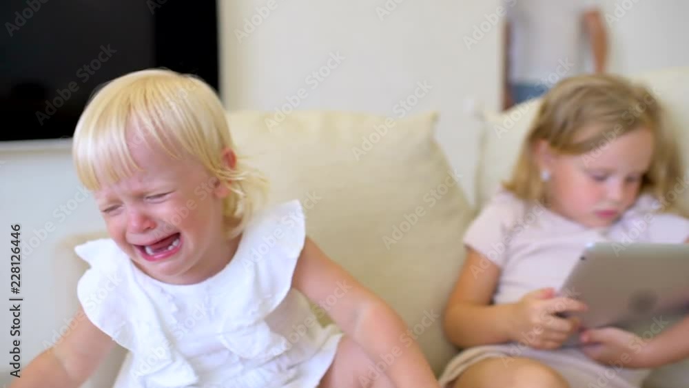 Little Girl Crying Using Tablet Two childs watching ang using tablet at home. Children using a modern ...