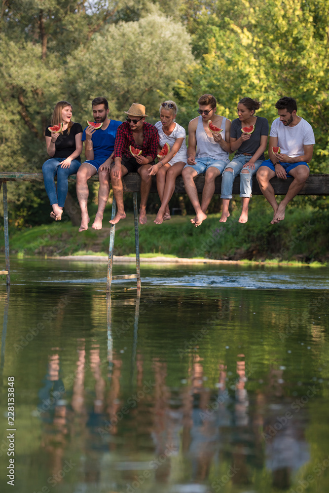 friends enjoying watermelon while sitting on the wooden bridge friends enjoying watermelon while sitting on the wooden bridge