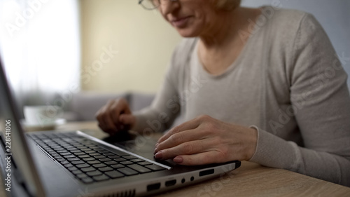 Old lady trying to type on laptop at home, computer courses, online training