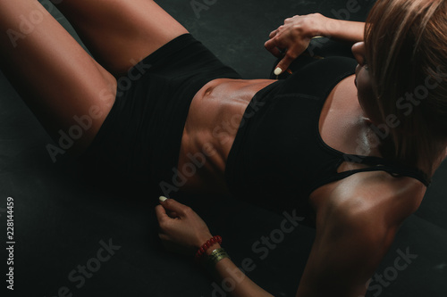 Athletic woman with strong muscular abs is sitting on black background in black sport sexy outfit  tanned skin  no face