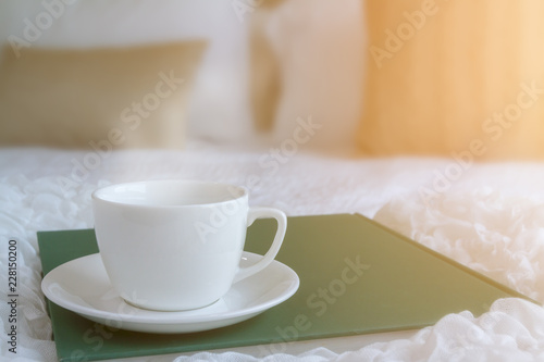 White coffee cup put on green plate in the bed room with soft streme smoke and window lighting. Background process by sunlight effect as a morning. Selective focus and copy space