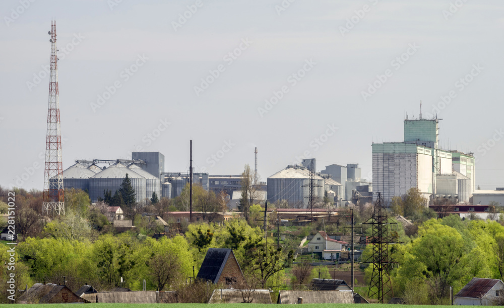 The village on the background of the agricultural complex, grain warehouse and communication tower.