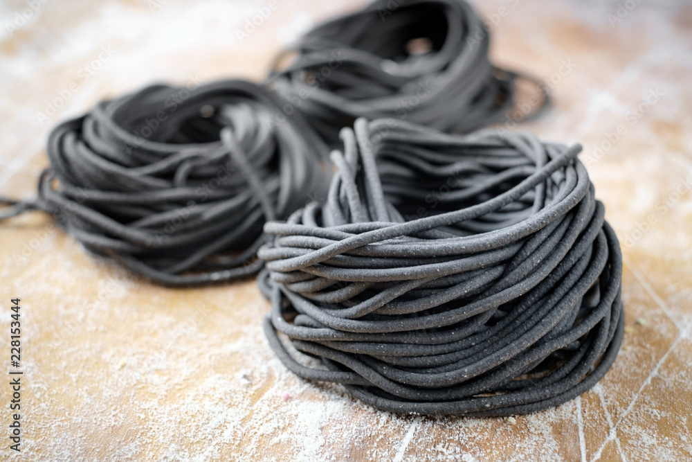Raw uncooked black spaghetti pasta homemade on a rustic wooden board Raw uncooked black spaghetti pasta homemade on a rustic wooden board