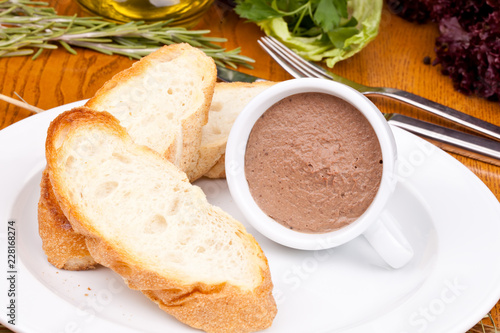 Chicken liver pate in cup and sliced baguette on white plate. Close up