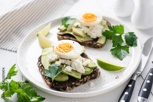 Healthy tasty toast with avocado, white cheese and boiled egg on white plate, closeup view, selective focus