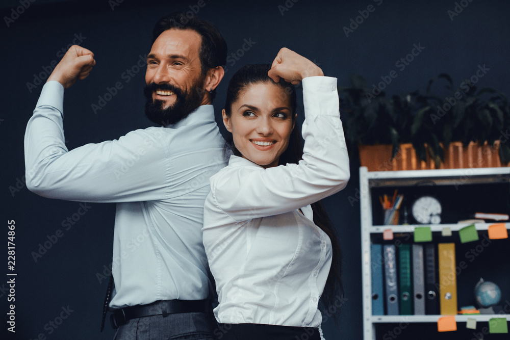 Smiling male and female colleagues demonstrate muscles on camera. Fight of genders concept. Smiling male and female colleagues demonstrate muscles on camera. Fight of genders concept.