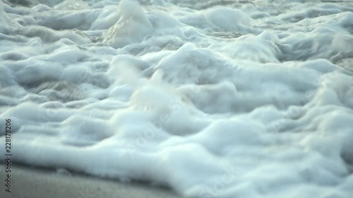 Surface of water sea ocean wave with white foam close-up on sand beach. Soft pastel blue tone. Concept rest relax summer recreation vacation holiday. Natural sea marine oceanic background backdrop photo