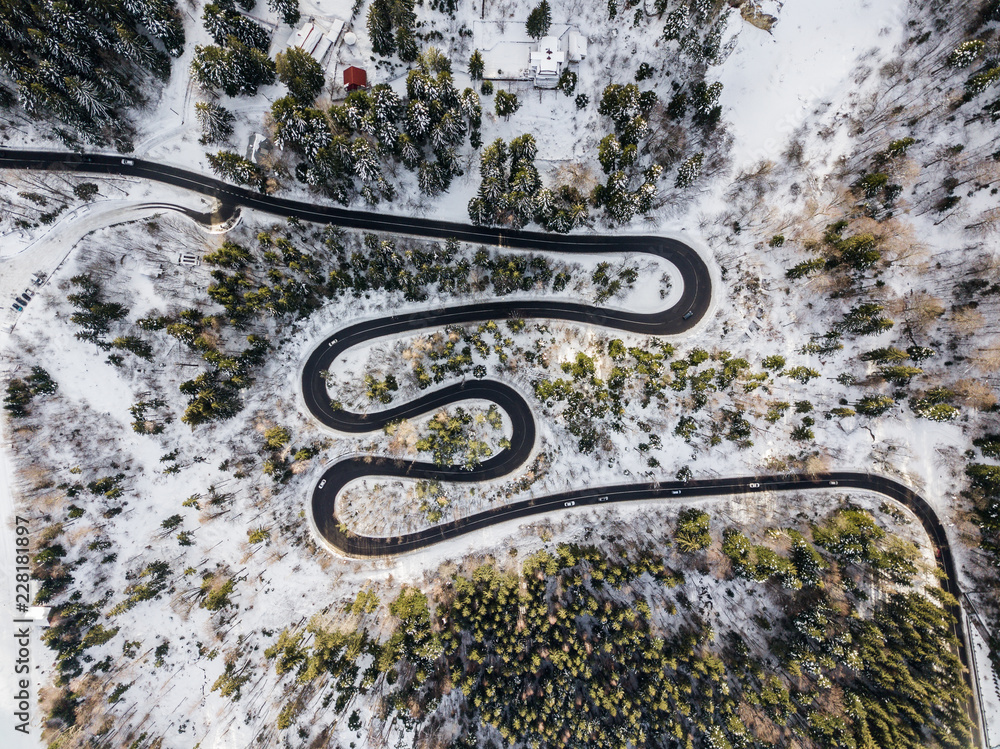 Winding road from high mountain pass, in winter time. Aerial view by drone . Romania