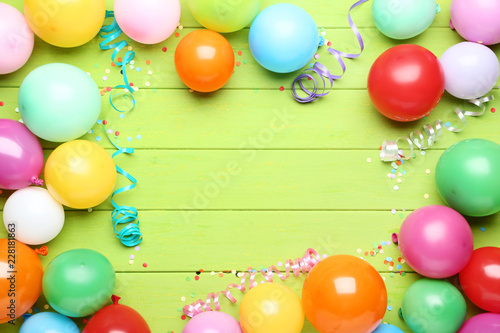 Colorful balloons with confetti on green wooden table