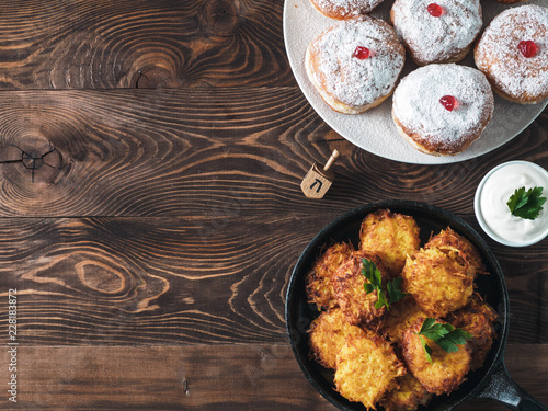 Jewish holiday Hanukkah concept and background. Hanukkah food doughnuts and potatoes pancakes latkes, oil and traditional spinnig dreidl on wooden table. Top view or flat lay. Copy space for text.