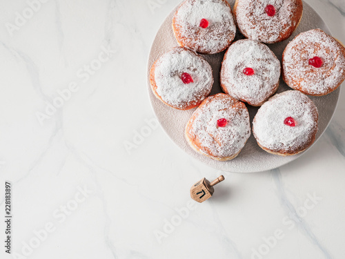 Jewish holiday Hanukkah concept and background. Hanukkah food doughnuts and traditional spinnig dreidl or dredel on white marble table background. Copy space for text. Shallow DOF.Top view or flat lay photo