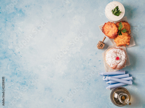 Jewish holiday Hanukkah concept and background. Hanukkah food doughnuts and potatoes pancakes latkes, oil and traditional spinnig dreidl on blue background. Top view or flat lay. Copy space for text.