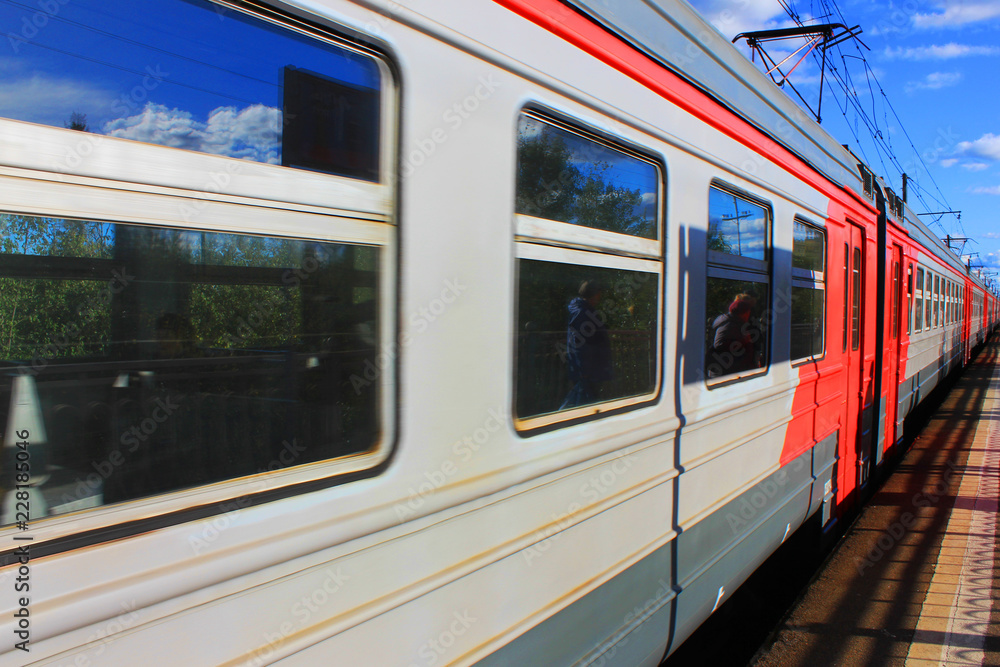 Local Train in Motion at Platform on Railway Station. Train Arriving at the Station on Summer Day. View of Old Grey and Red Train with Doors Closed and Sky Reflecting on the Windows