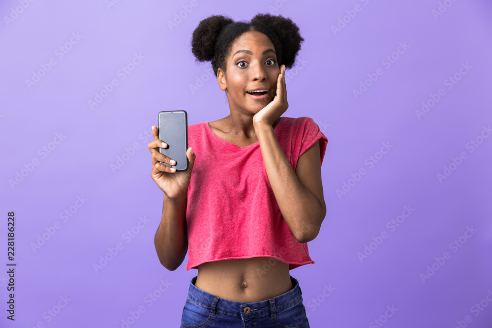 Photo of excited african american woman smiling and holding mobile phone, isolated over violet background Photo of excited african american woman smiling and holding mobile phone, isolated over violet background