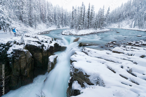 Cold scenery at Sunwapta Falls in the Canadian Rockies with snow and fir trees in wonderful scenery and ice and blue rivers running through the scenery with snowy hut © Thomas
