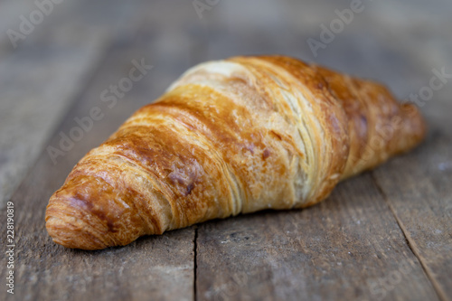 Tasty well-baked croissant on a wooden kitchen table. Light bread prepared for breakfast.