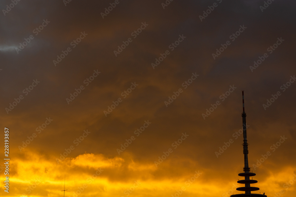 Silhouettes of radio tower and city houses  in front of dramatic red cloud formation