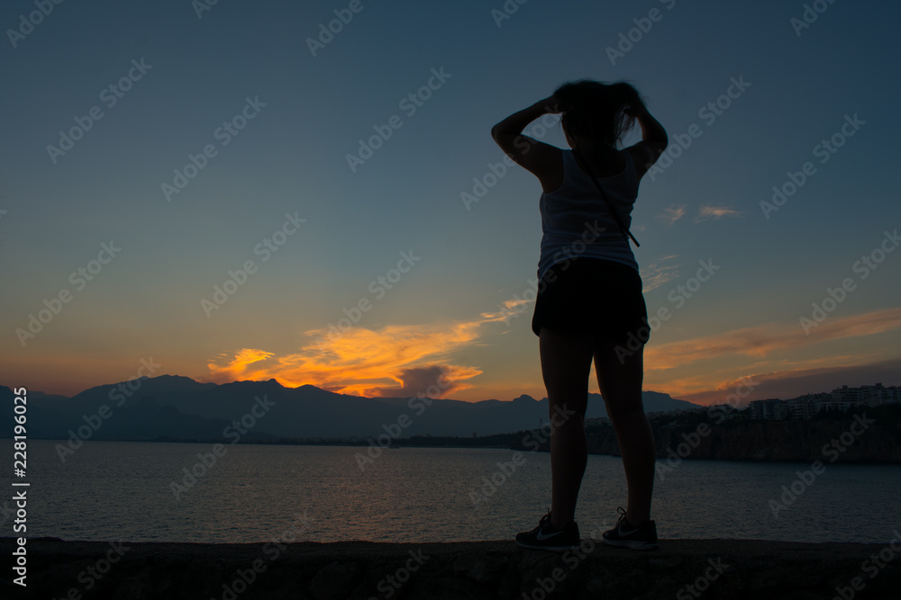 back view of young woman looking on beautiful sunset above sea and taurus mountains in Antalya, Turkey