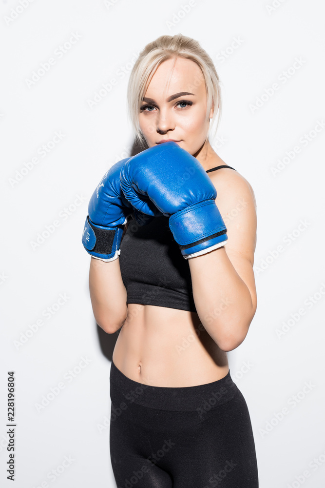 Beautiful smiling young fitness woman wears blue boxing gloves over grey background