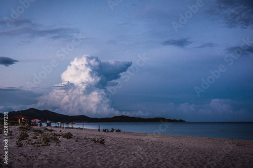 Empty beach at dusk in Costa Rei, Sardinia, Italy. Dramatic clouds in the blue hour that look like a shape of a giant dog. Mountains in the background.