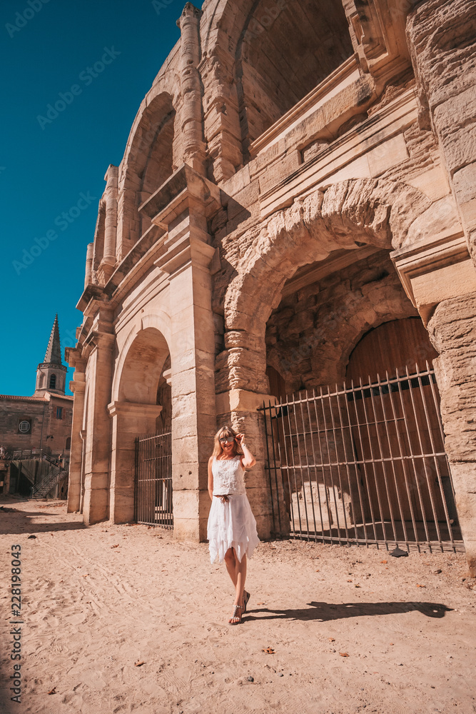 Arles, France, September 23, 2018: Beautiful slim attractive blonde tourist girl posing on Arles Amphitheater background