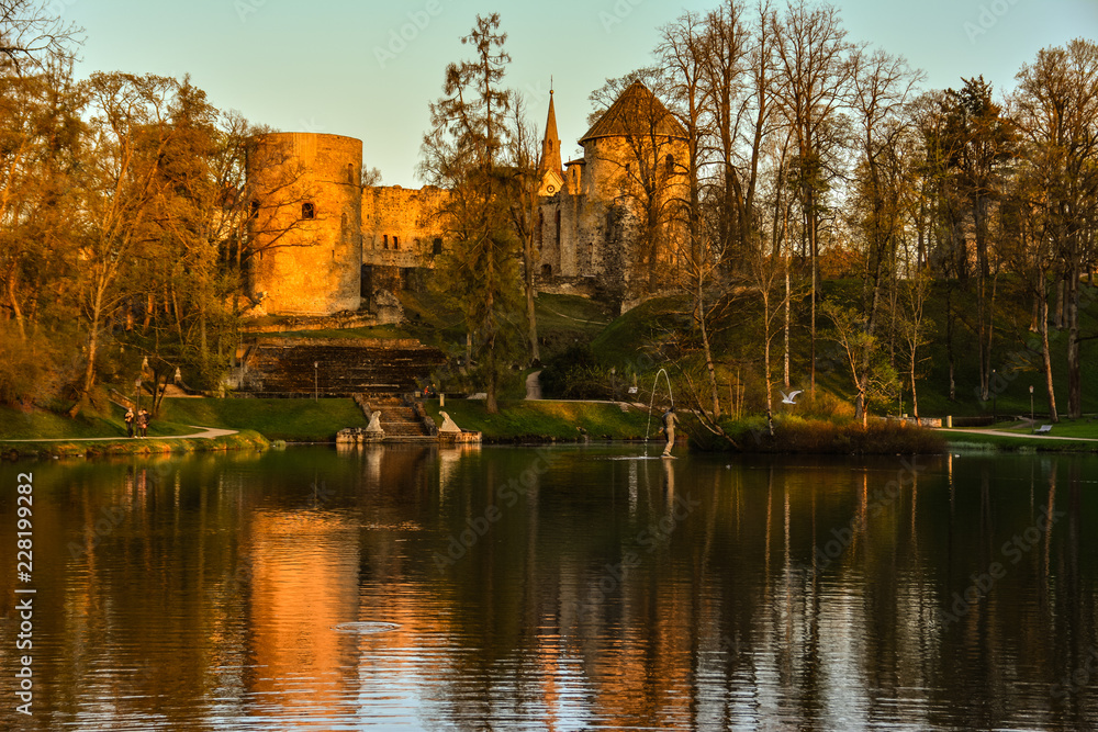 Beautiful afternoon light in public park with green grass and old medieval castle ruins reflecting in the pond. Shot in Cesis, Latvia.