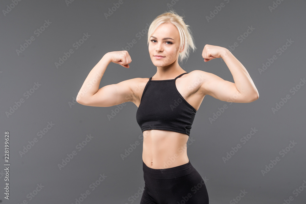 Young sporty woman looking at her biceps isolated on gray background Young sporty woman looking at her biceps isolated on gray background