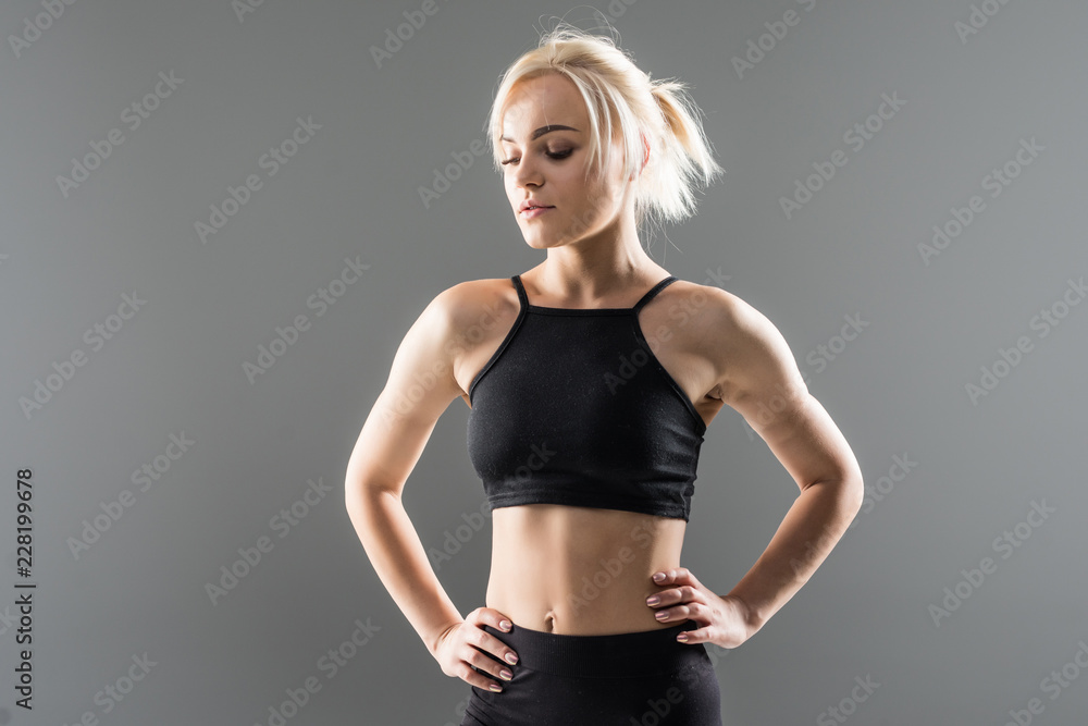 Portrait of sexy young woman with her hands on hips looking at camera. Fitness female with muscular body ready for workout on grey background