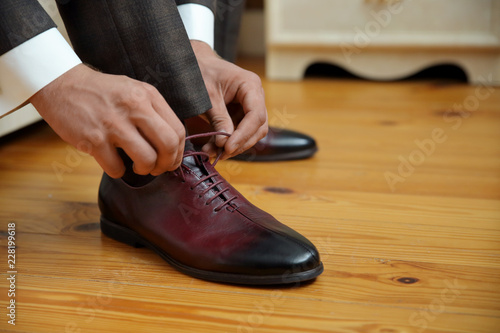 closed lacing, a man laces up his shoes on a wooden floor