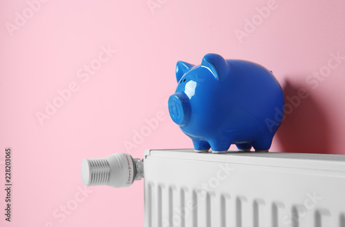 Heating radiator with piggy bank near color wall. Space for text