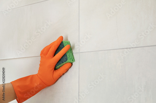 Woman in protective glove cleaning bathroom wall with sponge, closeup