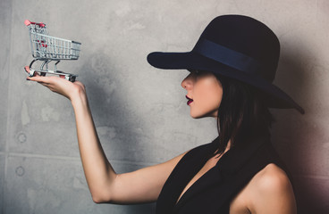 Portrait of a style brunette woman in hat with cart on grey background