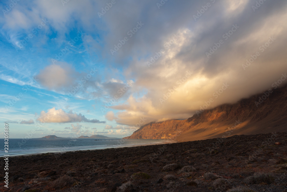 mountain with a cap of clouds on the ocean at sunset