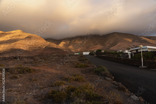 an asphalt road leading to the mountains swathed in fluffy clouds in the rays of the evening sun