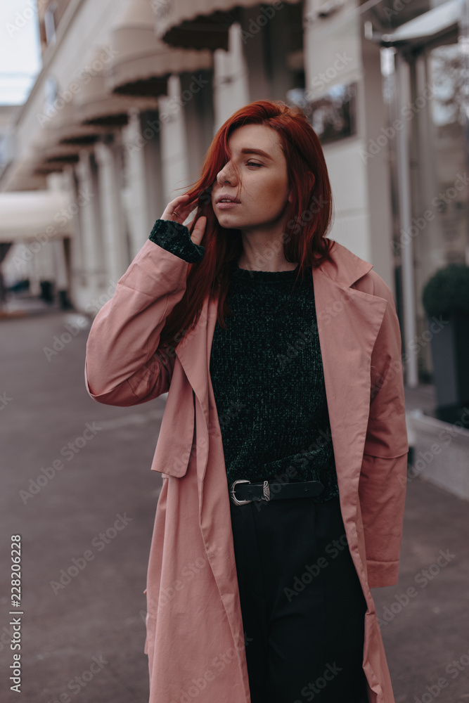 Beautiful and stylish girl with red hair walks in the city and her hair is in the wind Beautiful and stylish girl with red hair walks in the city and her hair is in the wind