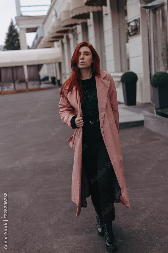 Naklejka premium Beautiful and stylish girl with red hair walks in the city and her hair is in the wind