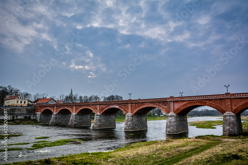 Famous old red brick bridge of Kuldiga, Latvia. There is a Venta river flowing under the bridge and salmon jumping in the river.