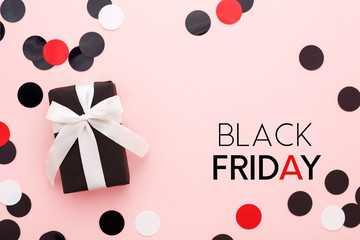 Black friday card. Black gift box with white bow and confetti on pink background. Top view, copy space, minimal.